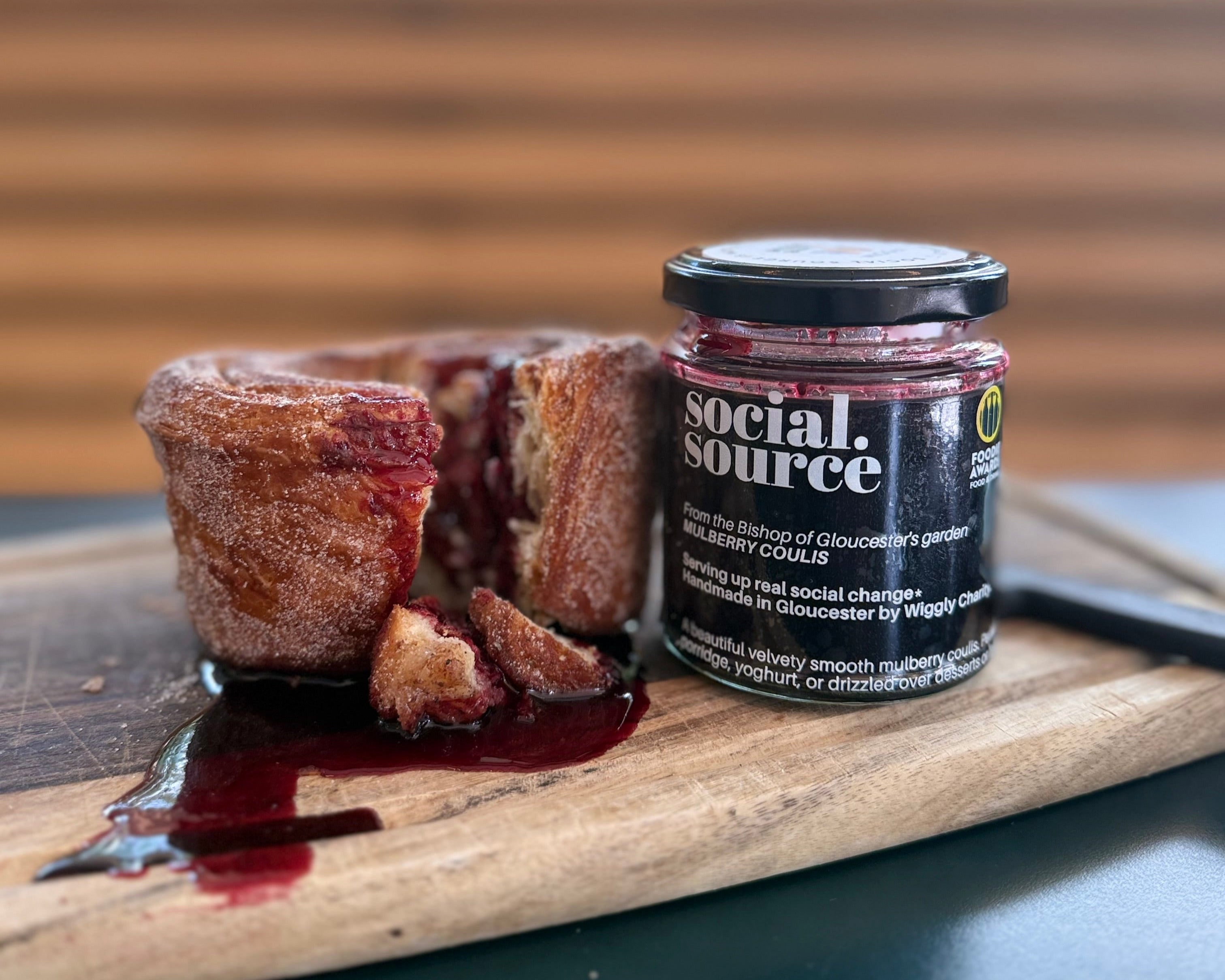 Jar of Social Source jam on a wooden board with a dessert